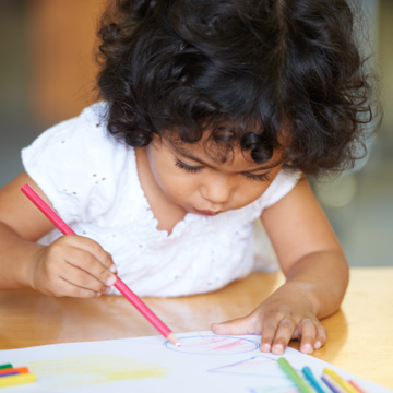 little girl writing on paper with a colored pencil