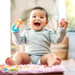 baby smiling on carpet with toy in his hand