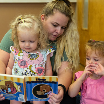 teacher sitting with kids on her lap reading a book